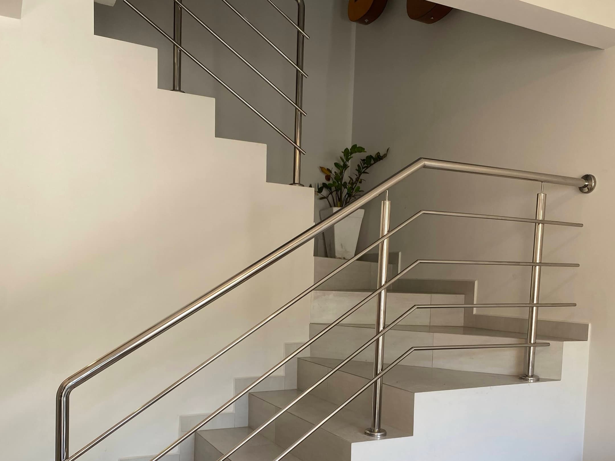 Guarda-corpo de inox com tubos horizontais e corrimão contínuo, acompanhando escada de porcelanato com patamar