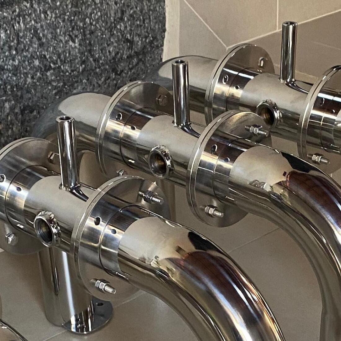 Curvas de tubo de inox polido com flanges de fixação, refletindo como espelho