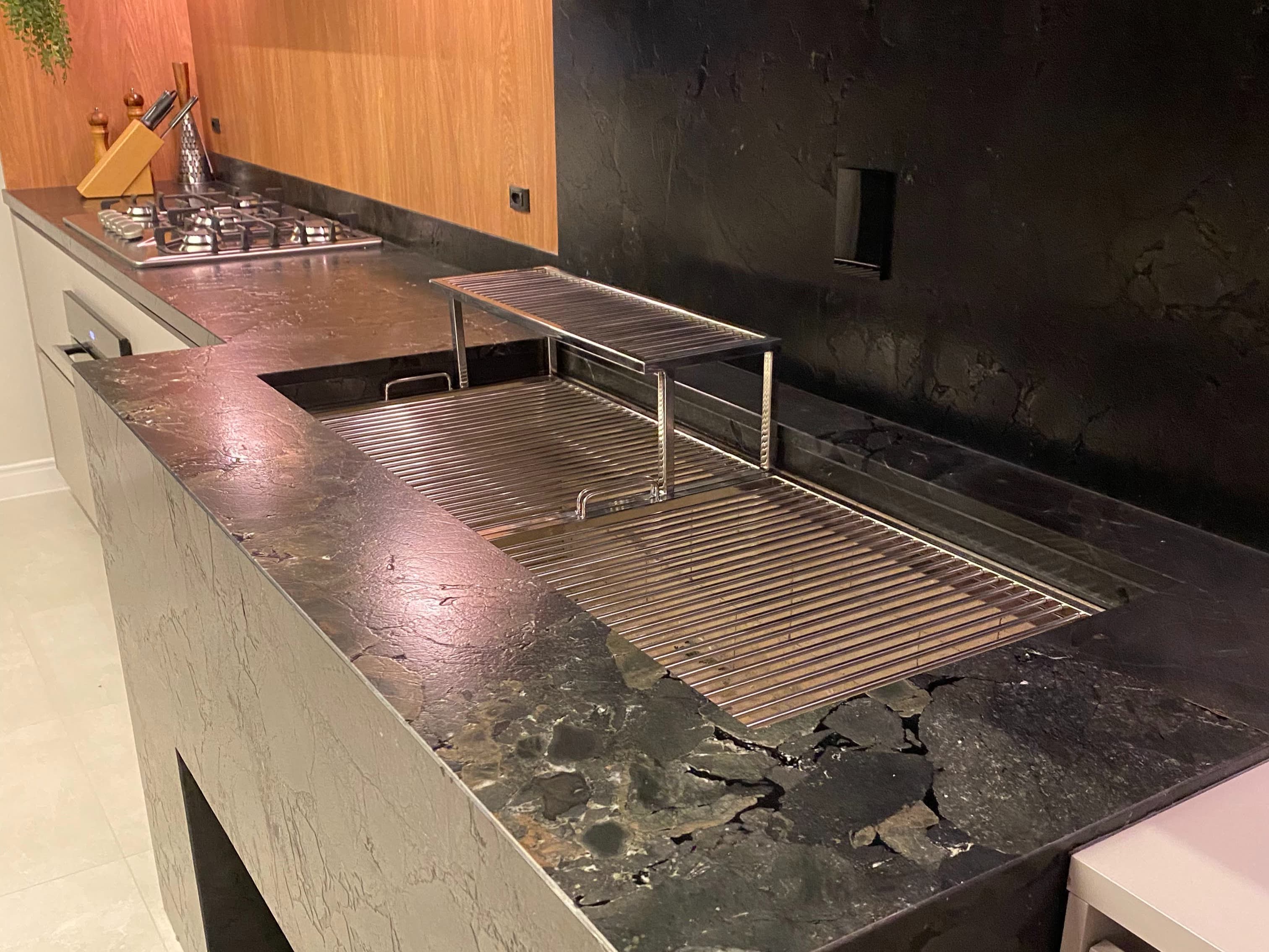 Vista da bancada completa, com a grelha de inox na posição elevada e cooktop a gás na mesma linha