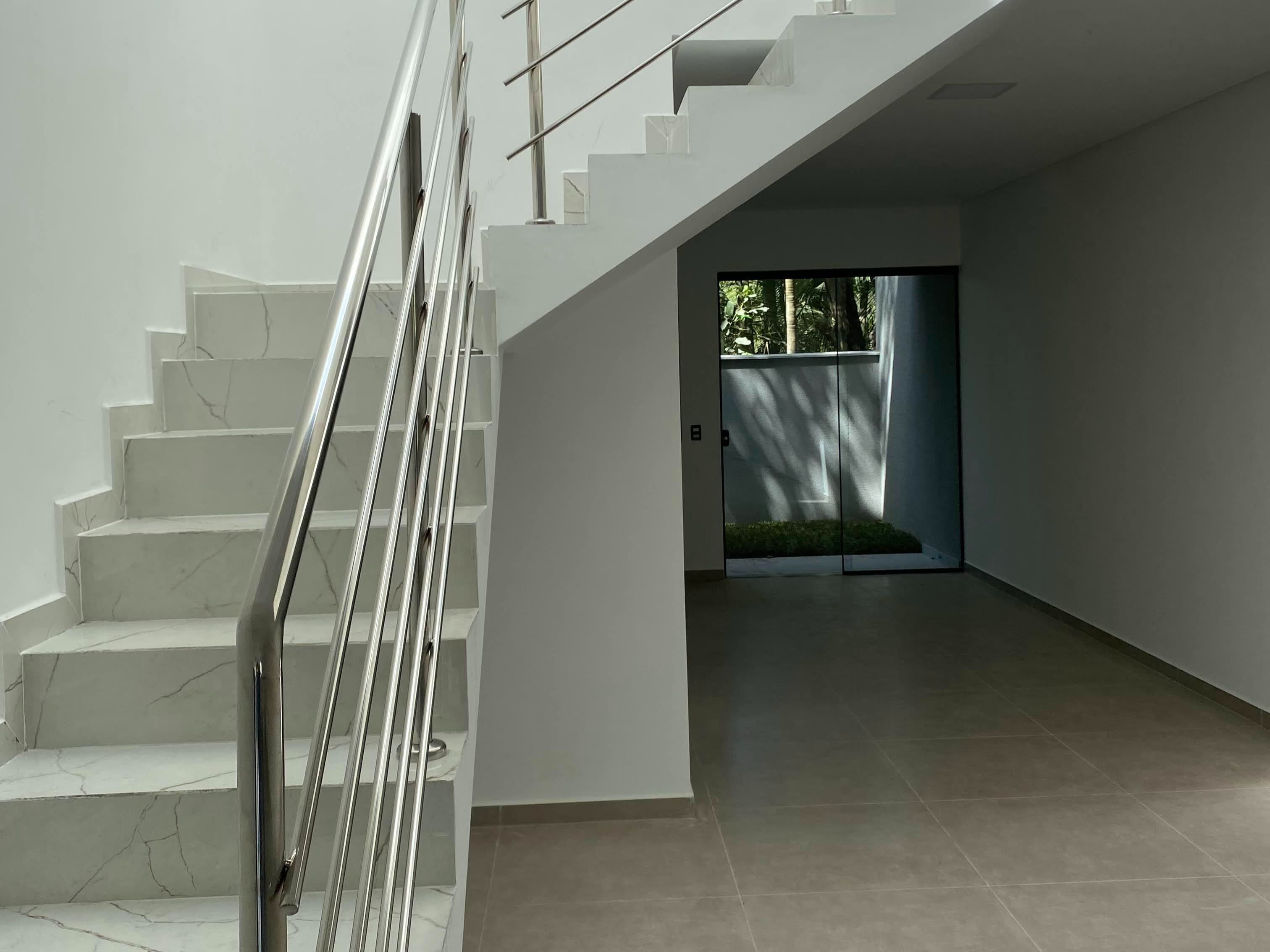 A escada vista do corredor, com o guarda-corpo de inox acompanhando os degraus de mármore